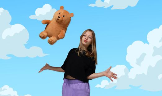 Teen girl throwing a teddy bear plush mascot toy in air, illustration of clouds and sky in background