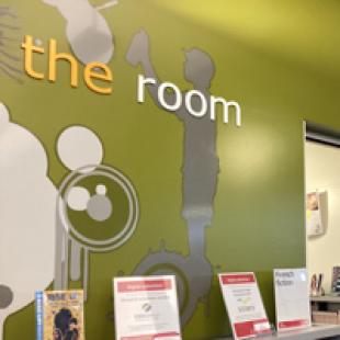 the words "the room" adorn the wall of the library near the entrance to the teen space