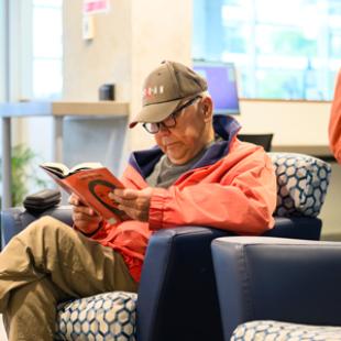 a man in an orange jacket sitting in an armchair in the library, reading a book 