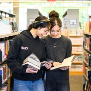 two teenage girls browsing for books in the library.